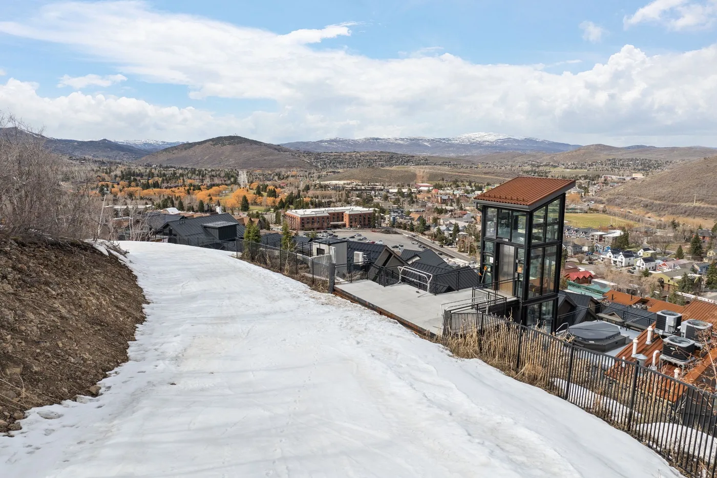 Un camino nevado al aire libre ofrece vistas de un pueblo y las colinas.