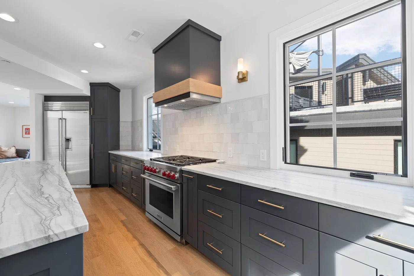 Una cocina moderna con gabinetes oscuros, una estufa y una encimera larga bajo grandes ventanas.