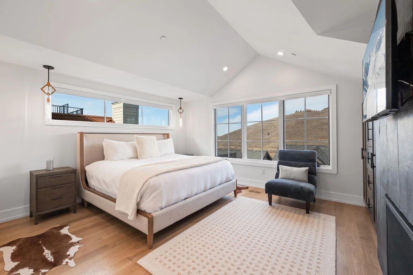 Un dormitorio luminoso con una cama, un sillón y ventanas amplias.