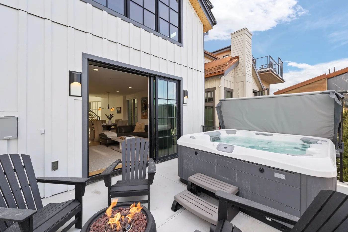Un patio exterior con una bañera de hidromasaje, asientos y una fogata junto a la casa.