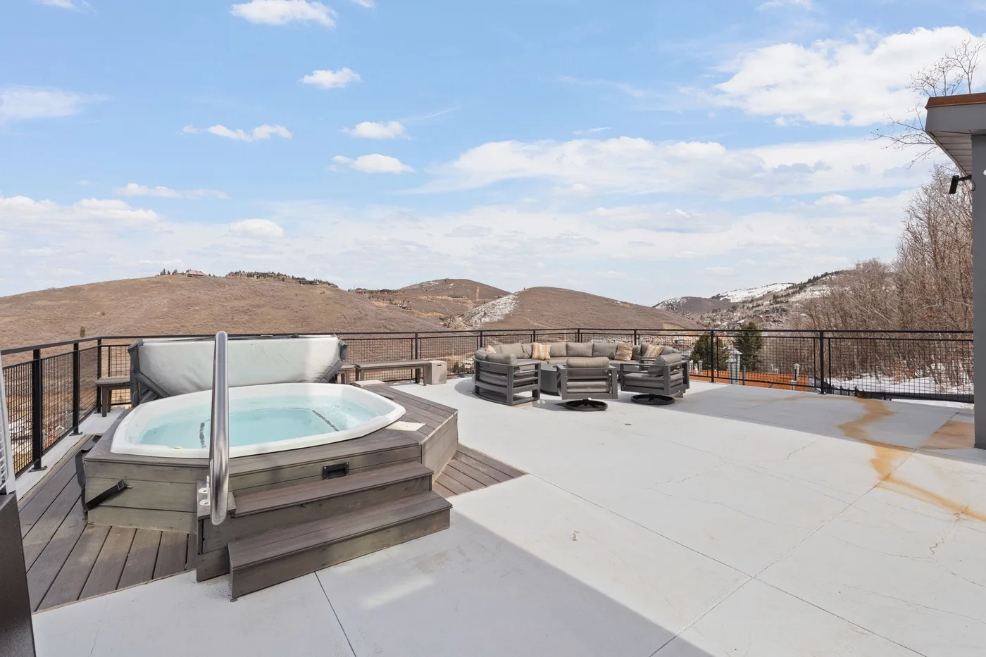 Una terraza en la azotea con una bañera de hidromasaje y asientos al aire libre tiene vistas a colinas.