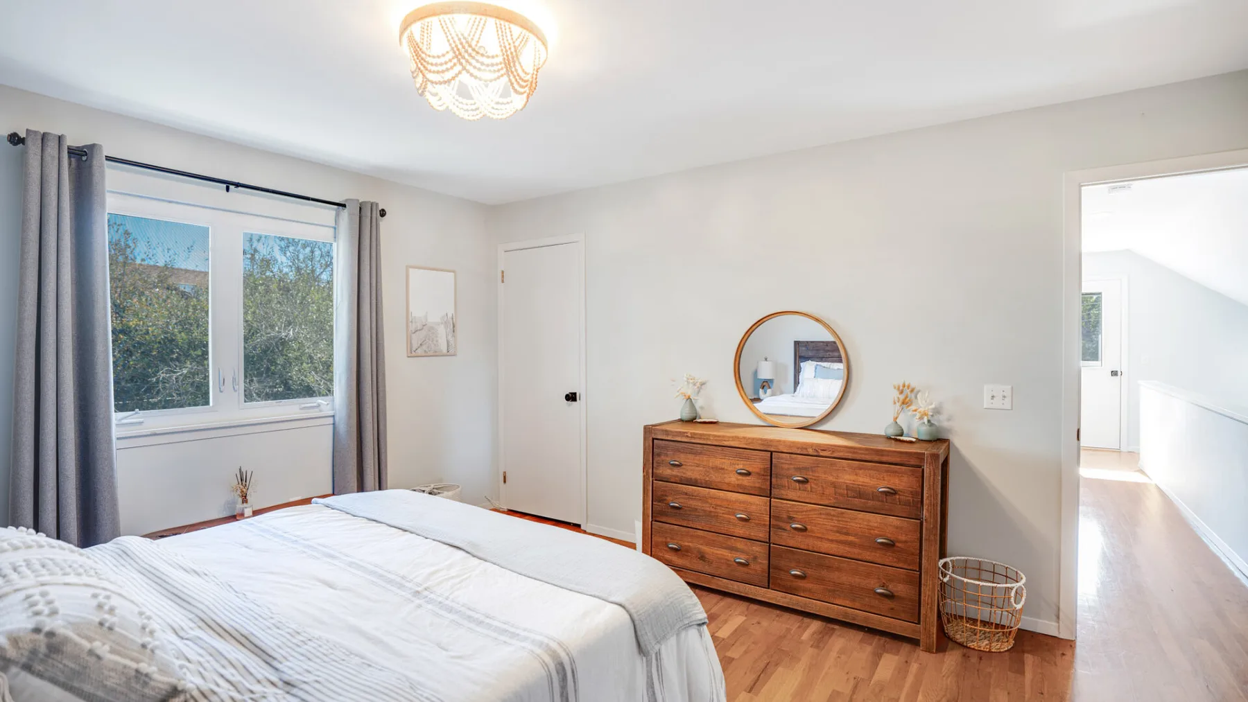 A bedroom with a bed, wooden dresser, and a window with gray curtains.