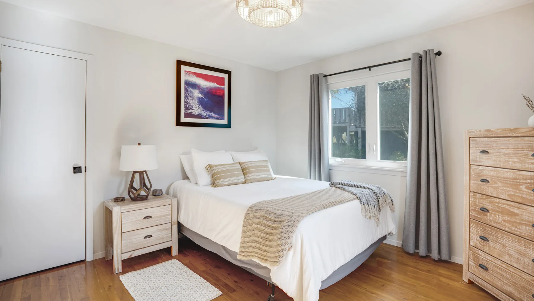 A bright bedroom with a bed, bedside table, and window.