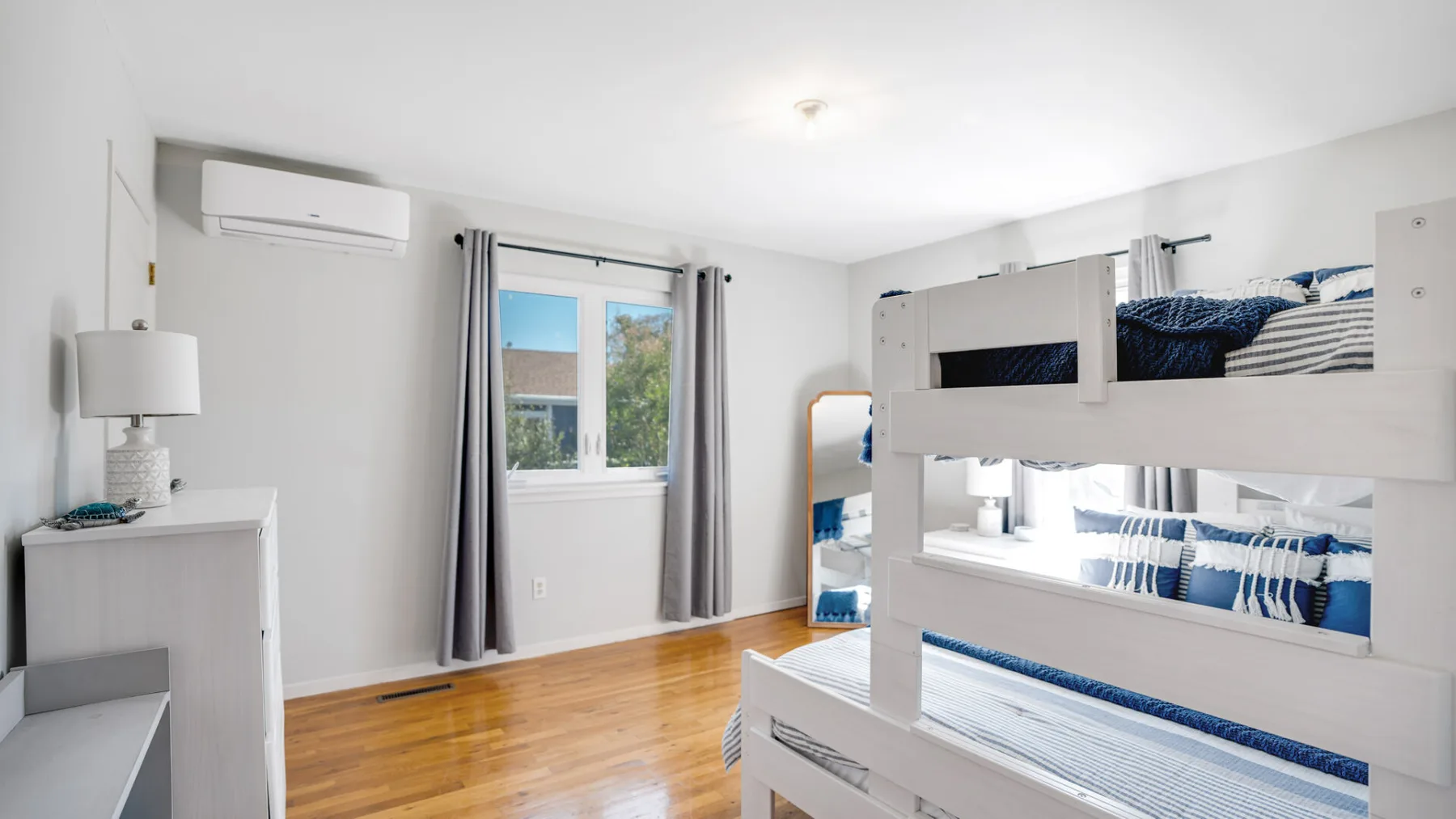 A bright bedroom with white bunk beds, blue bedding, and a window.
