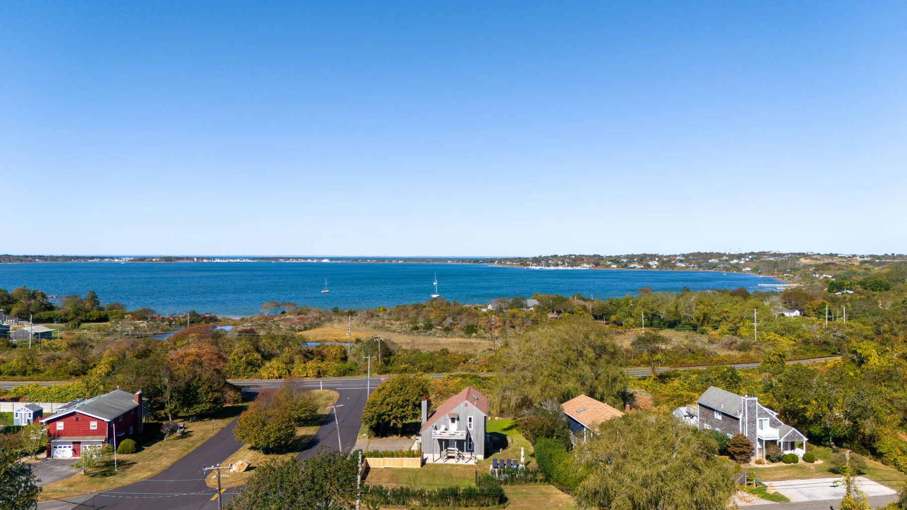 A coastal neighborhood with homes, trees, and blue water beyond.