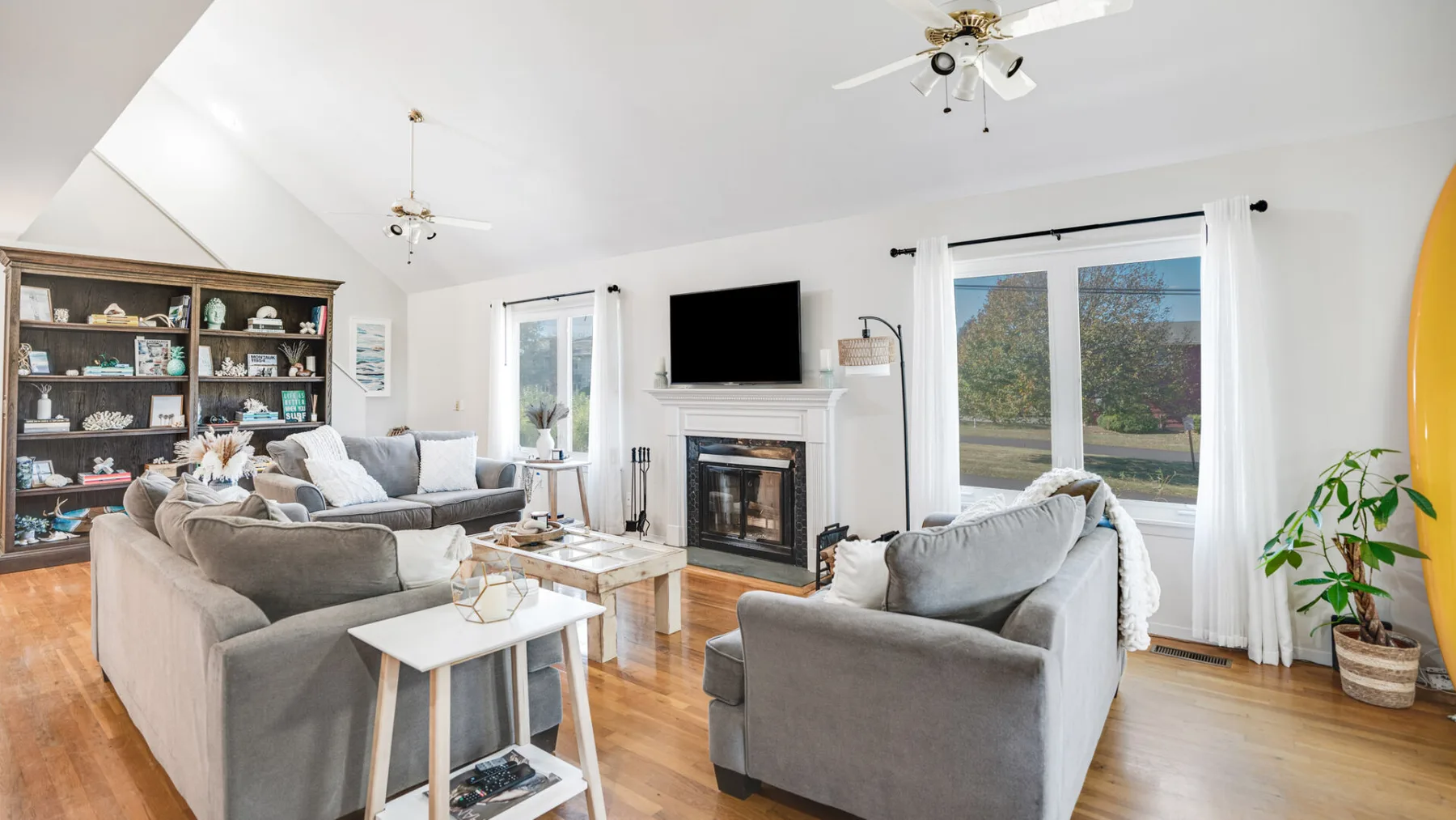 A bright living room with gray seating, a fireplace, and large windows.