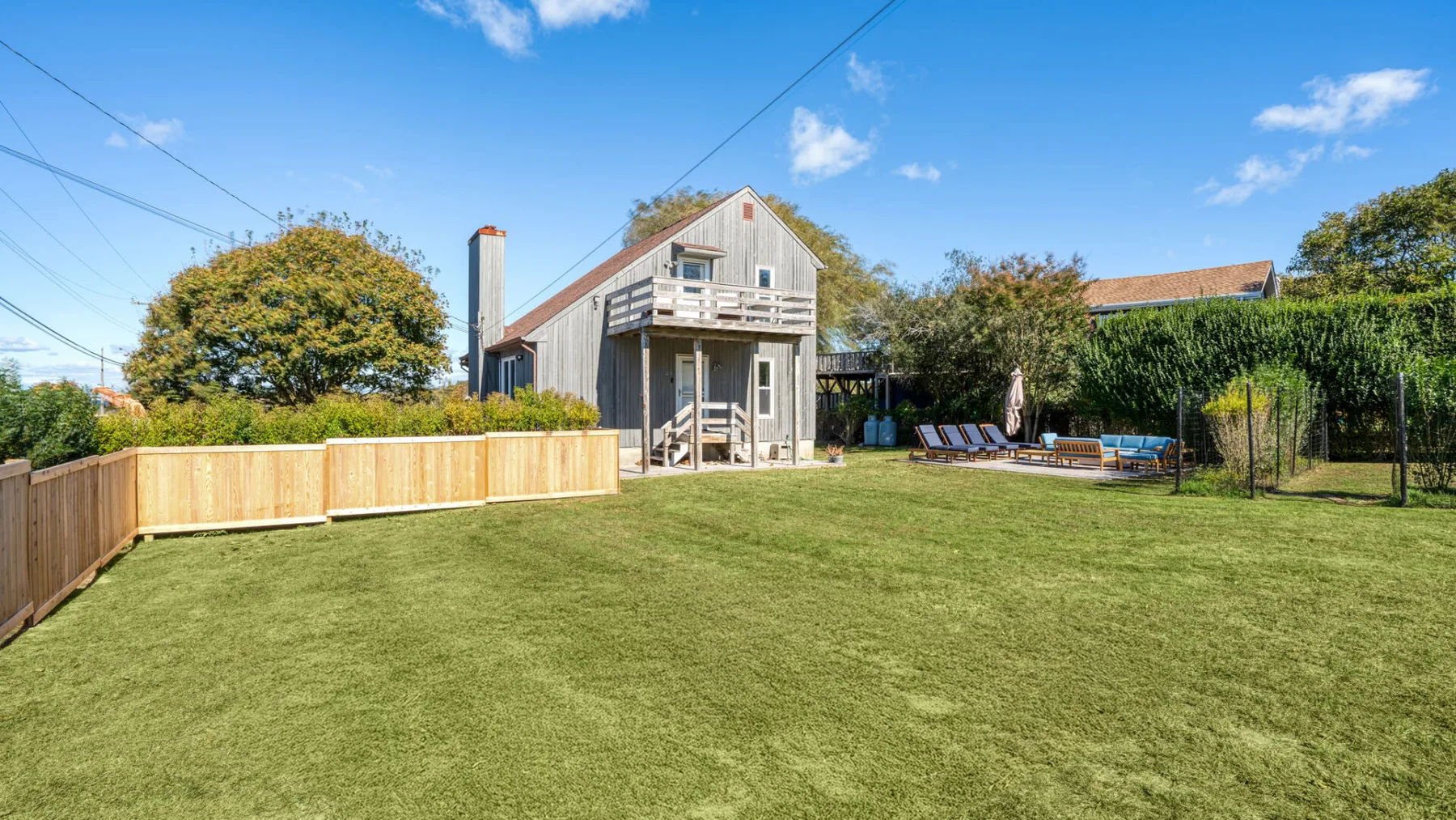 A fenced backyard with a broad lawn and a raised wooden playhouse.