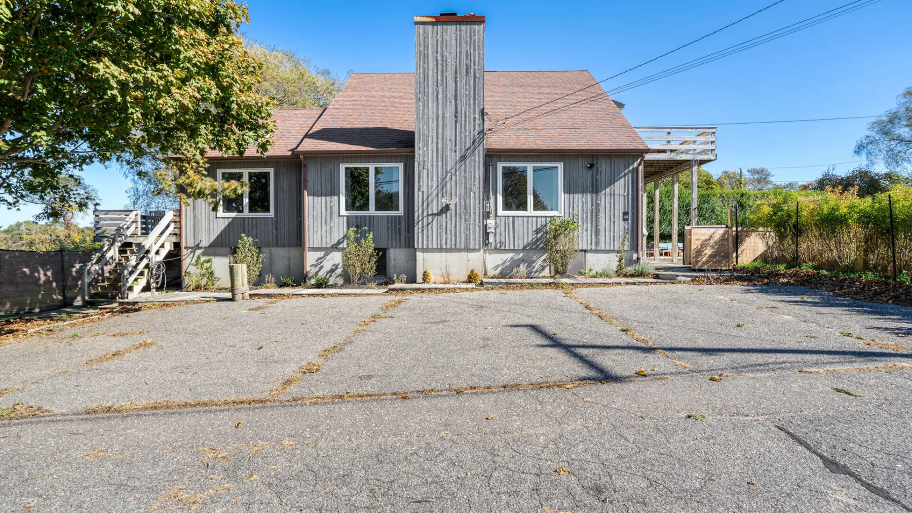 A gray house with a central chimney faces a paved parking area.