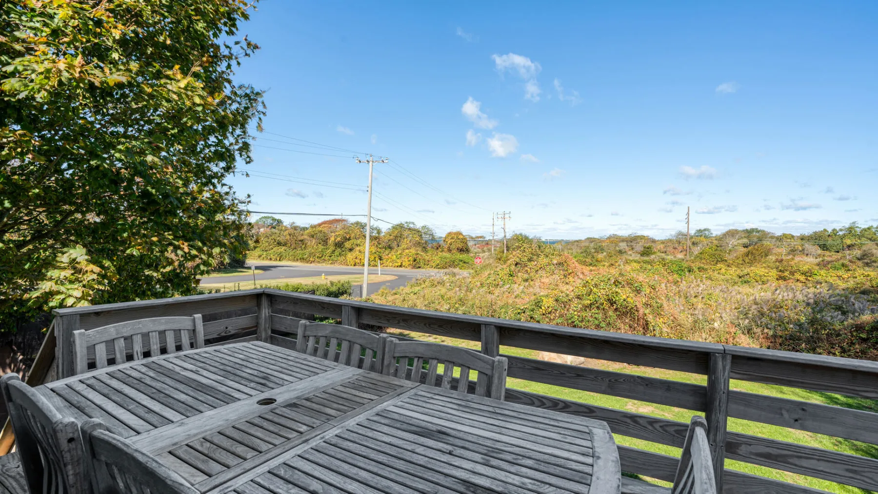 An outdoor deck with a long wooden table overlooks open greenery.