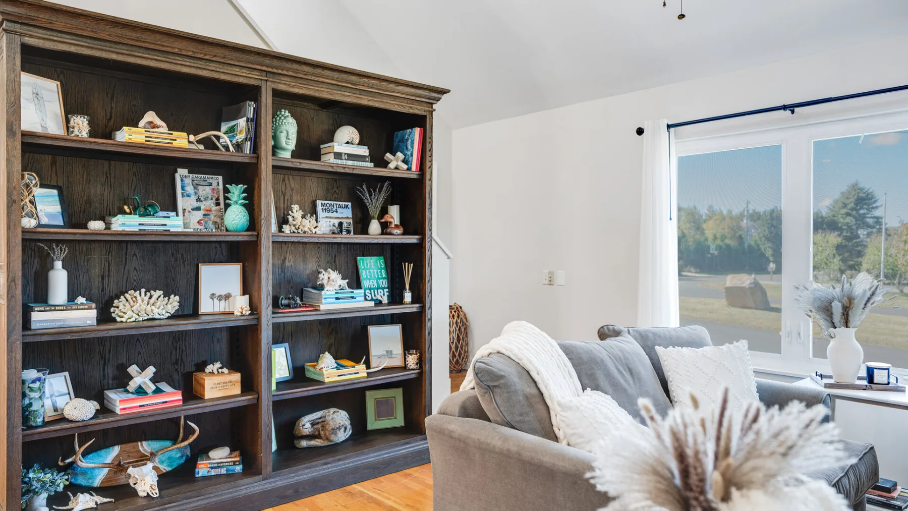 A bright living room with a large bookcase and seating beside a window.