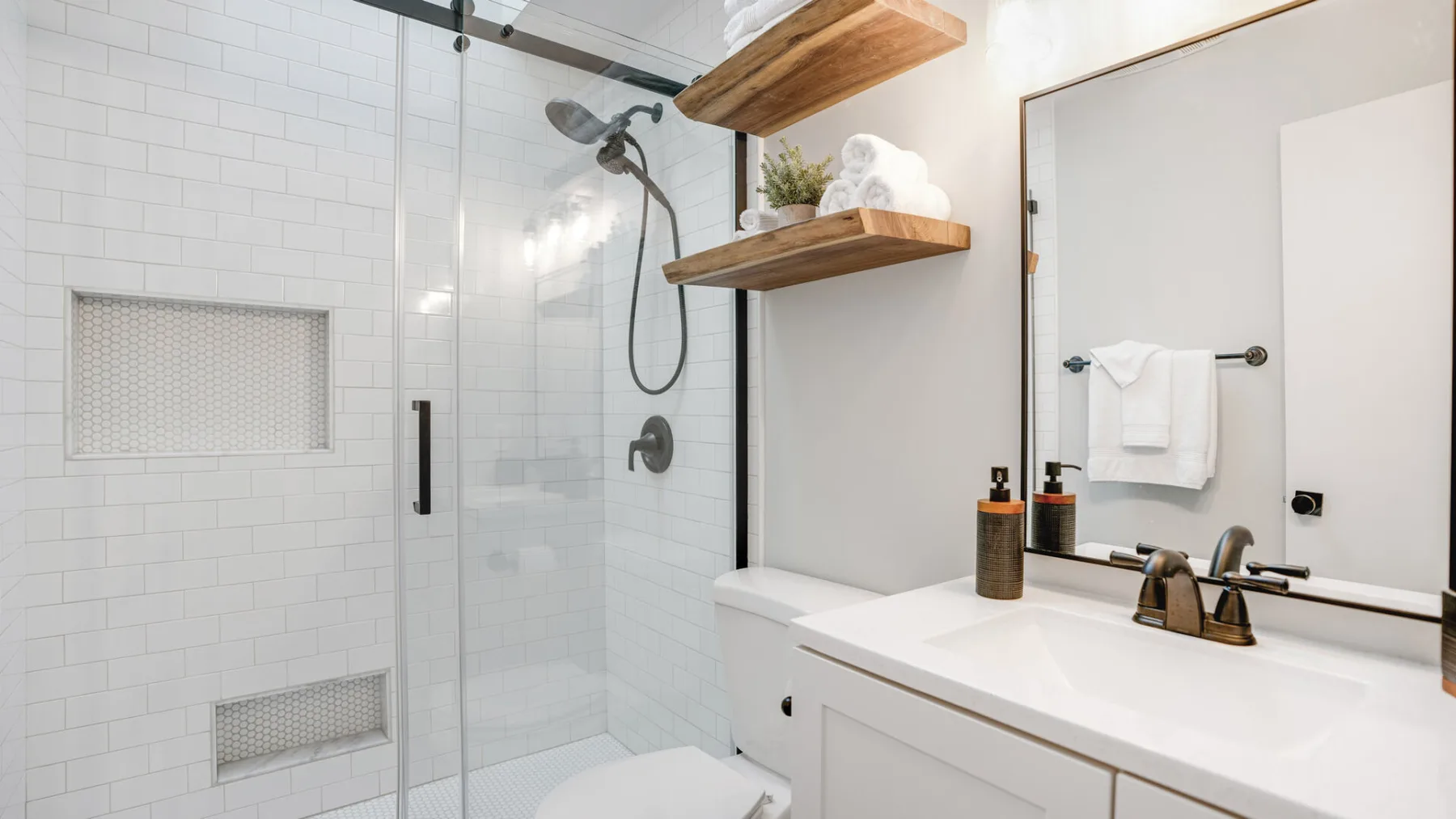 A bright tiled bathroom with a glass shower and a wide vanity.