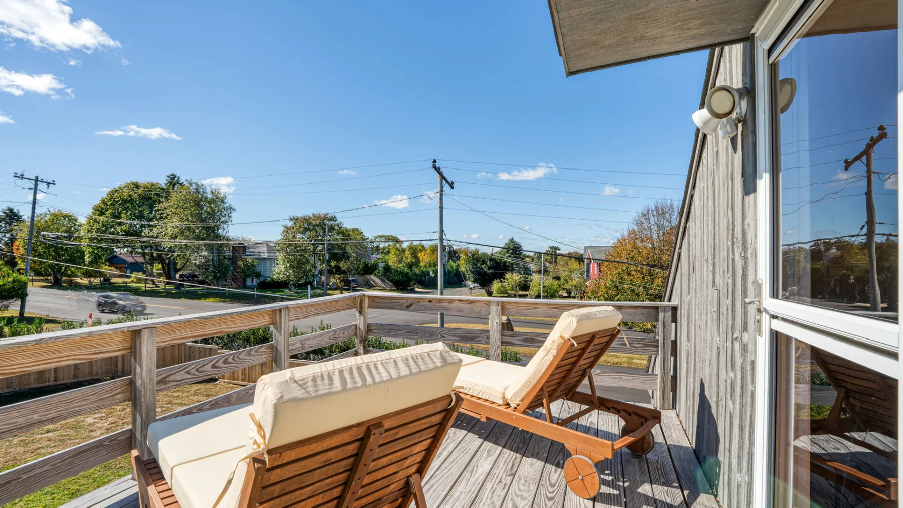 A wooden deck with cushioned lounge seating overlooks a tree-lined street.