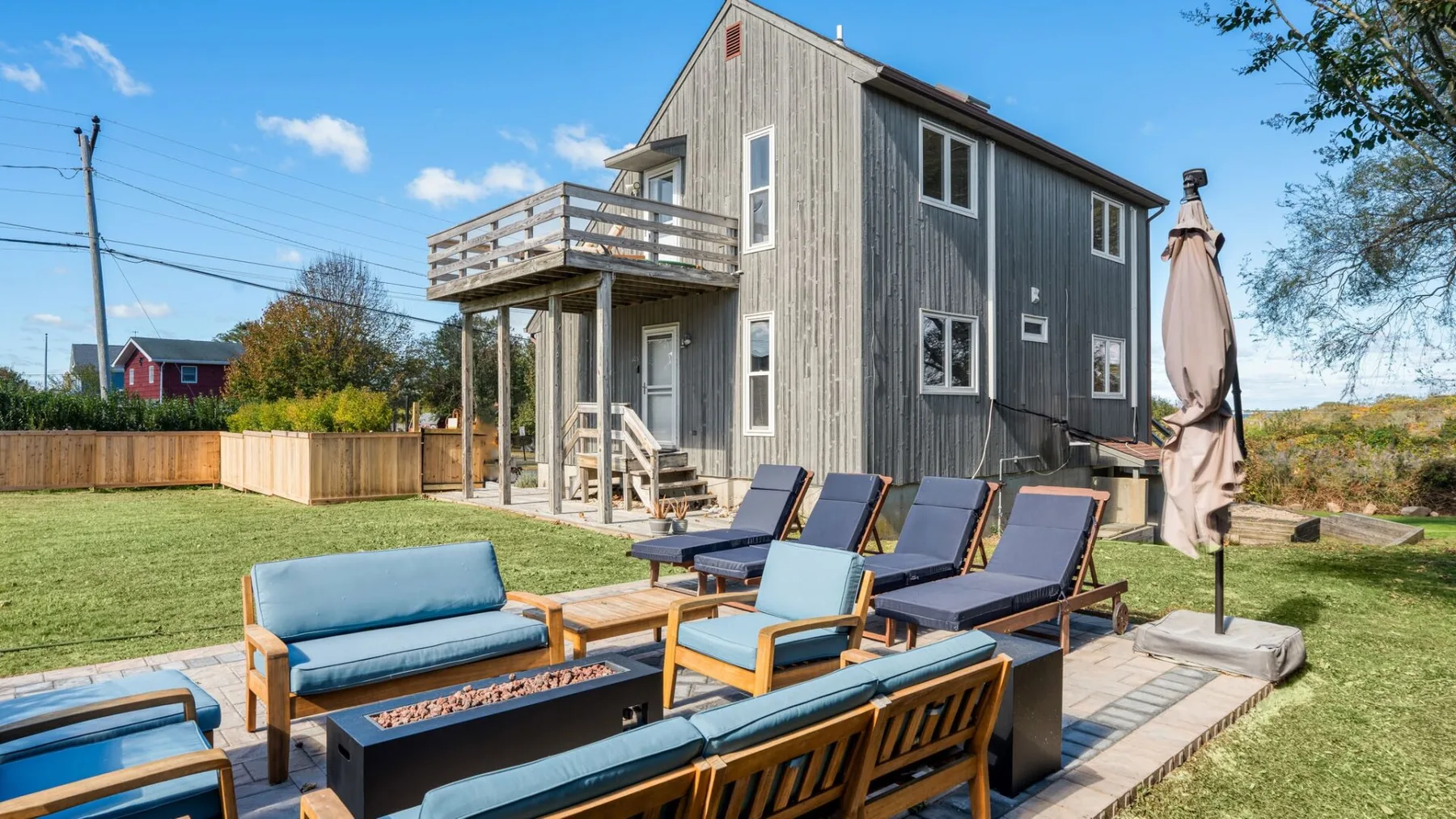 A raised house beside a patio with outdoor seating and a closed umbrella.