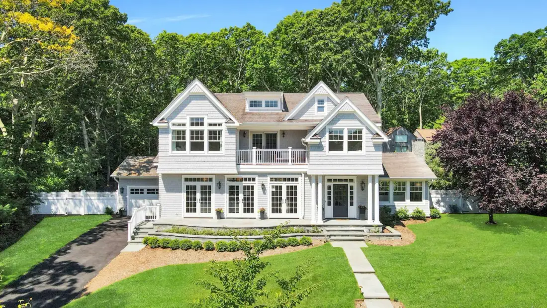 A large house stands behind a green lawn and a paved walkway.