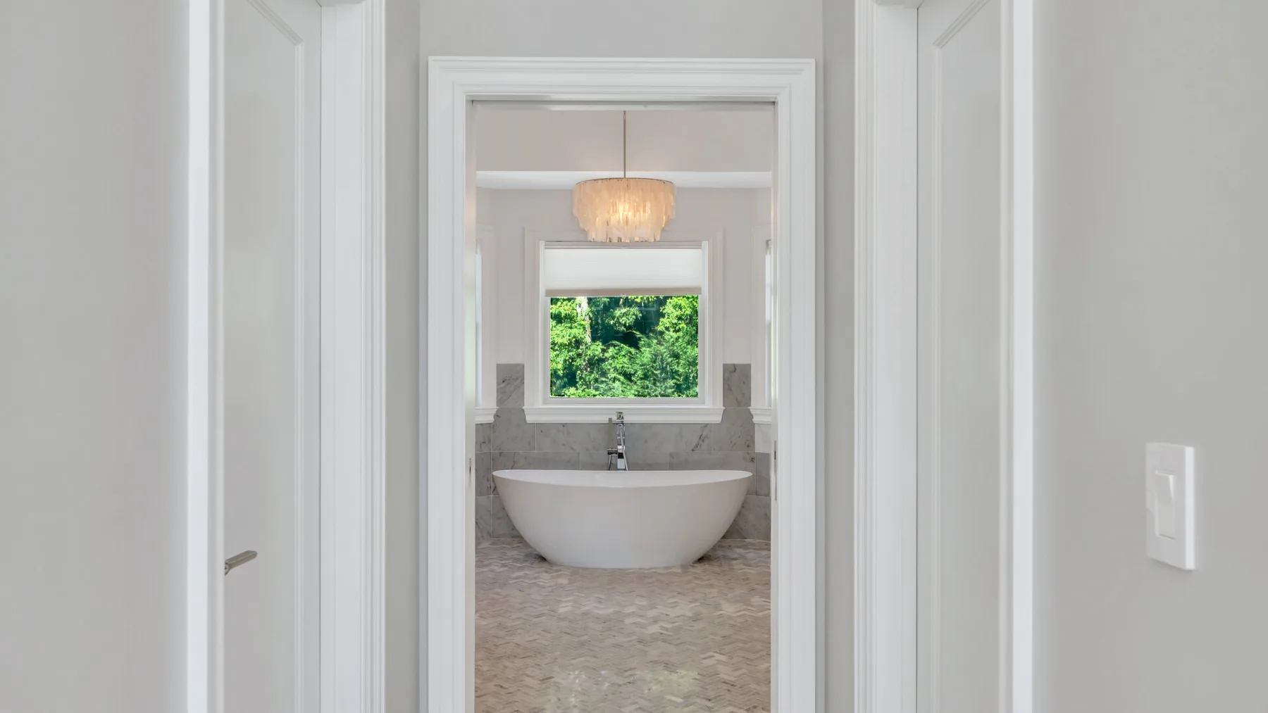 A bathroom with a freestanding tub beneath a window overlooking greenery.