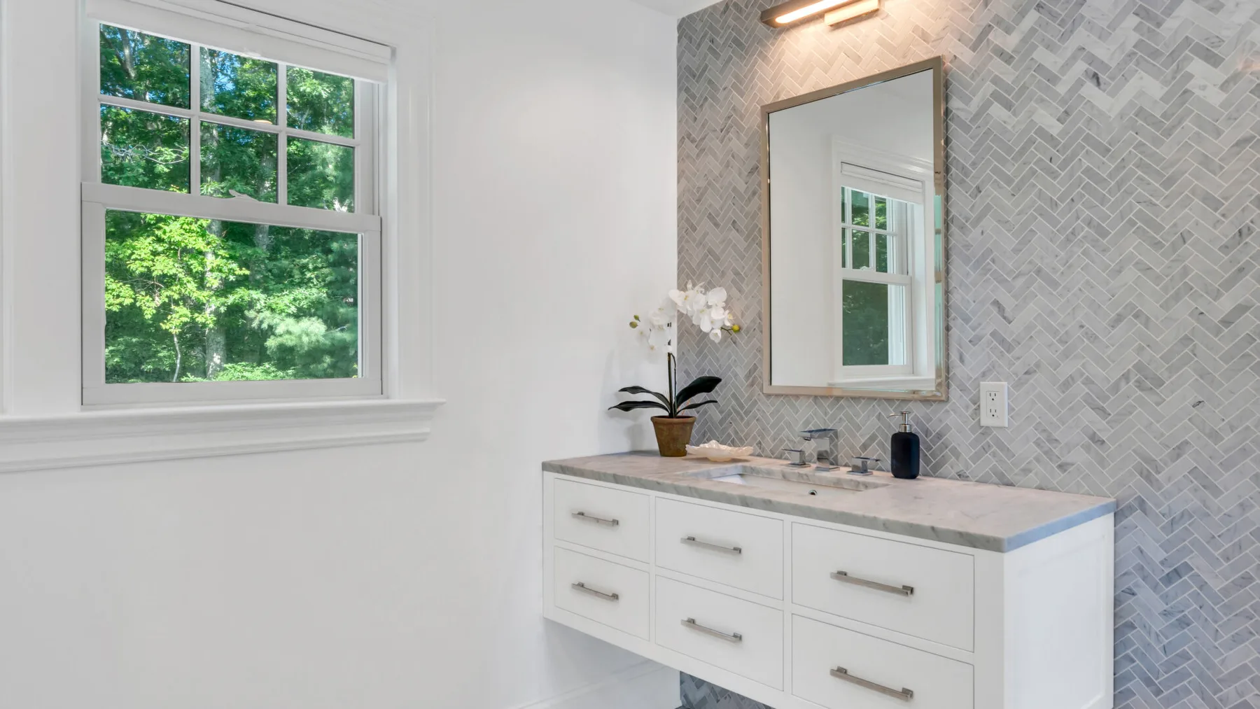 A bright bathroom vanity sits beside a window overlooking green trees.