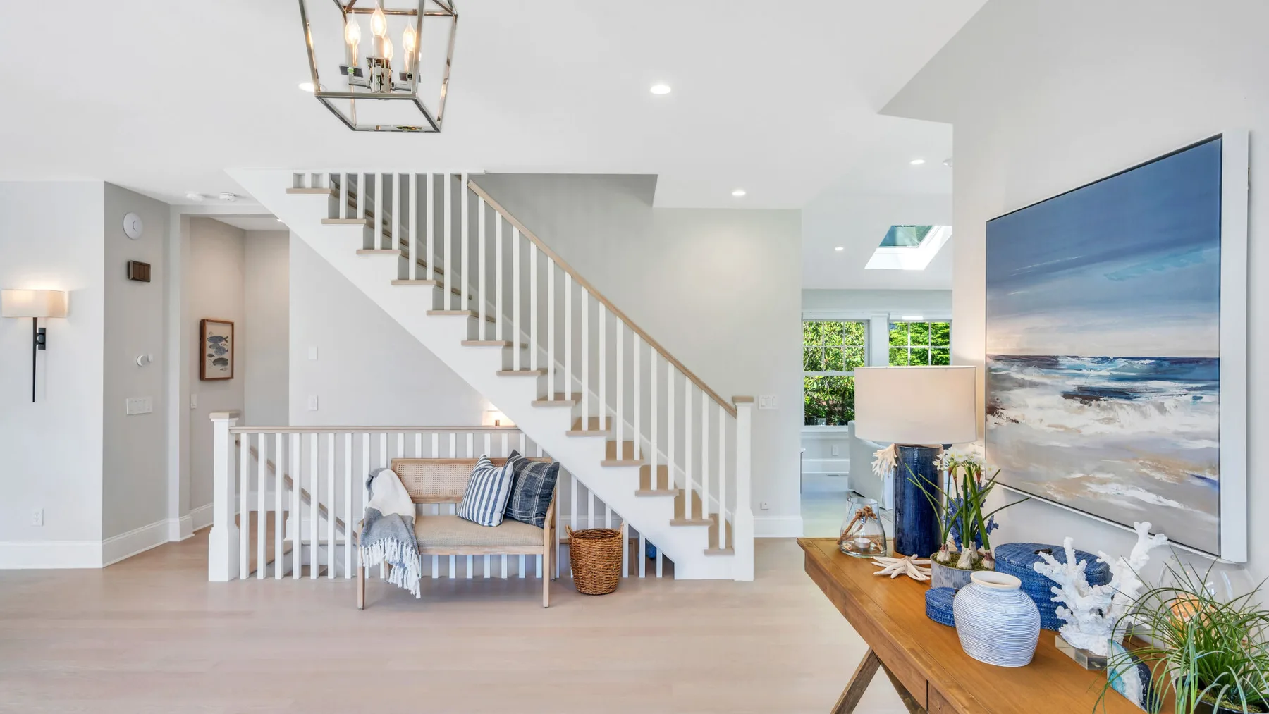 A bright living area with a bench beneath a staircase and large coastal artwork.