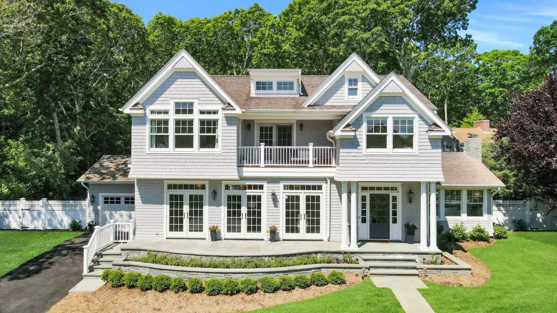 A large two-story house with white siding stands beside a green lawn.