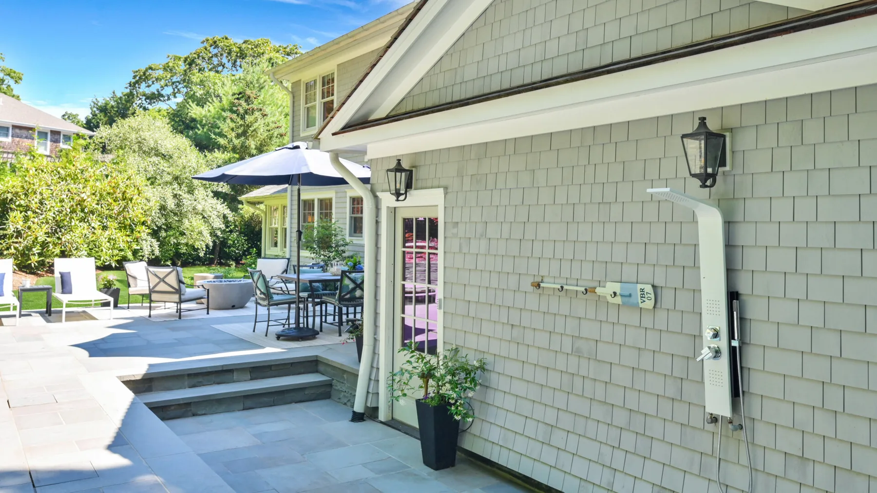 A paved outdoor patio beside a house, with seating and a shaded dining area.
