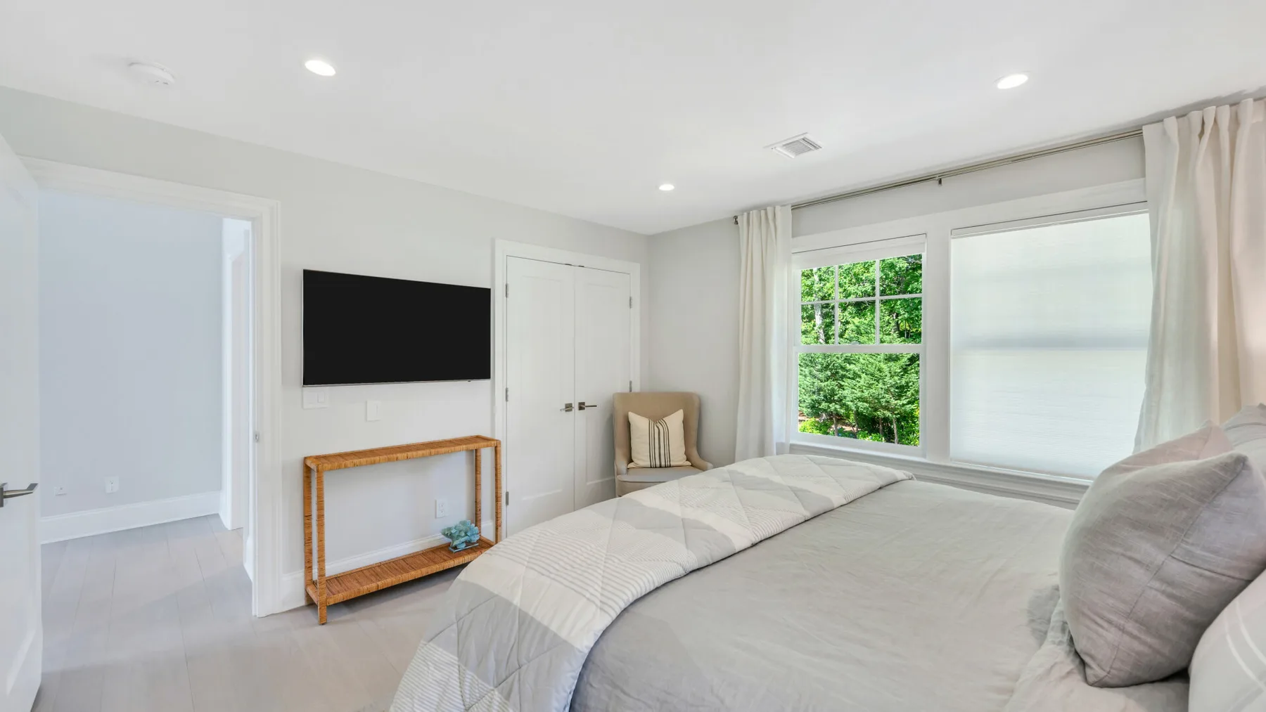 A bright bedroom with a bed, wall-mounted television, and large windows.