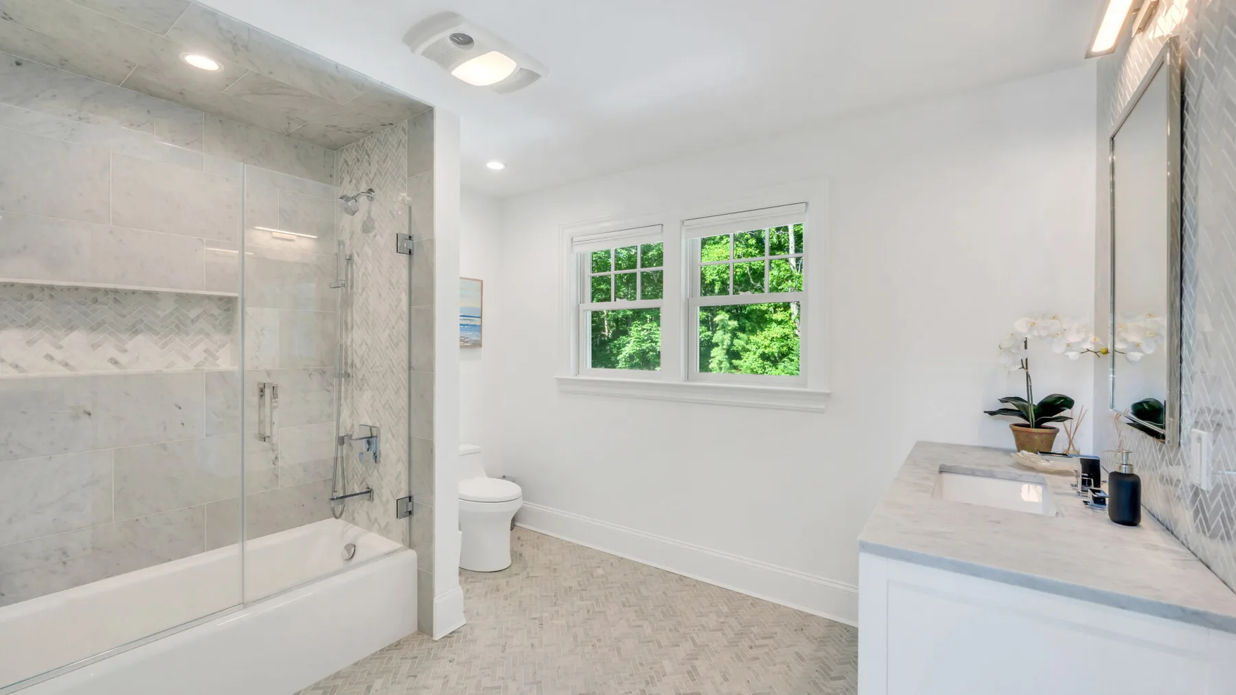 A bright bathroom with a glass shower, bathtub, and vanity.