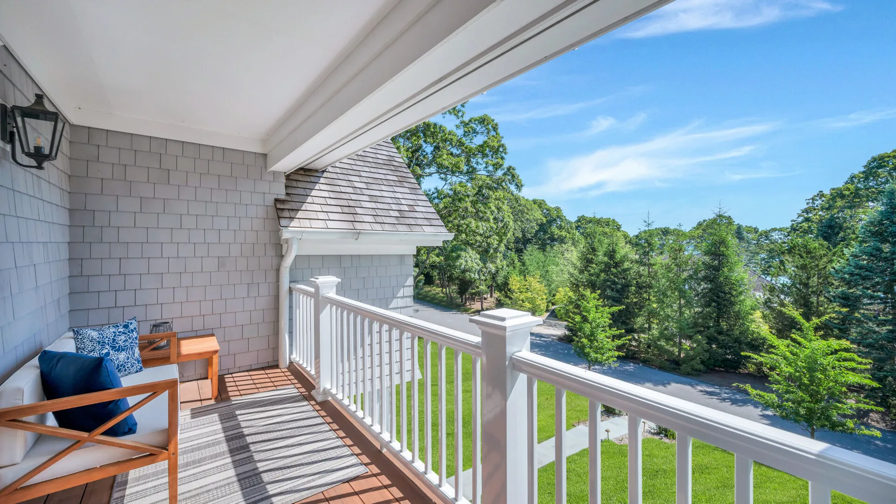 A covered balcony with seating overlooks a tree-lined road.