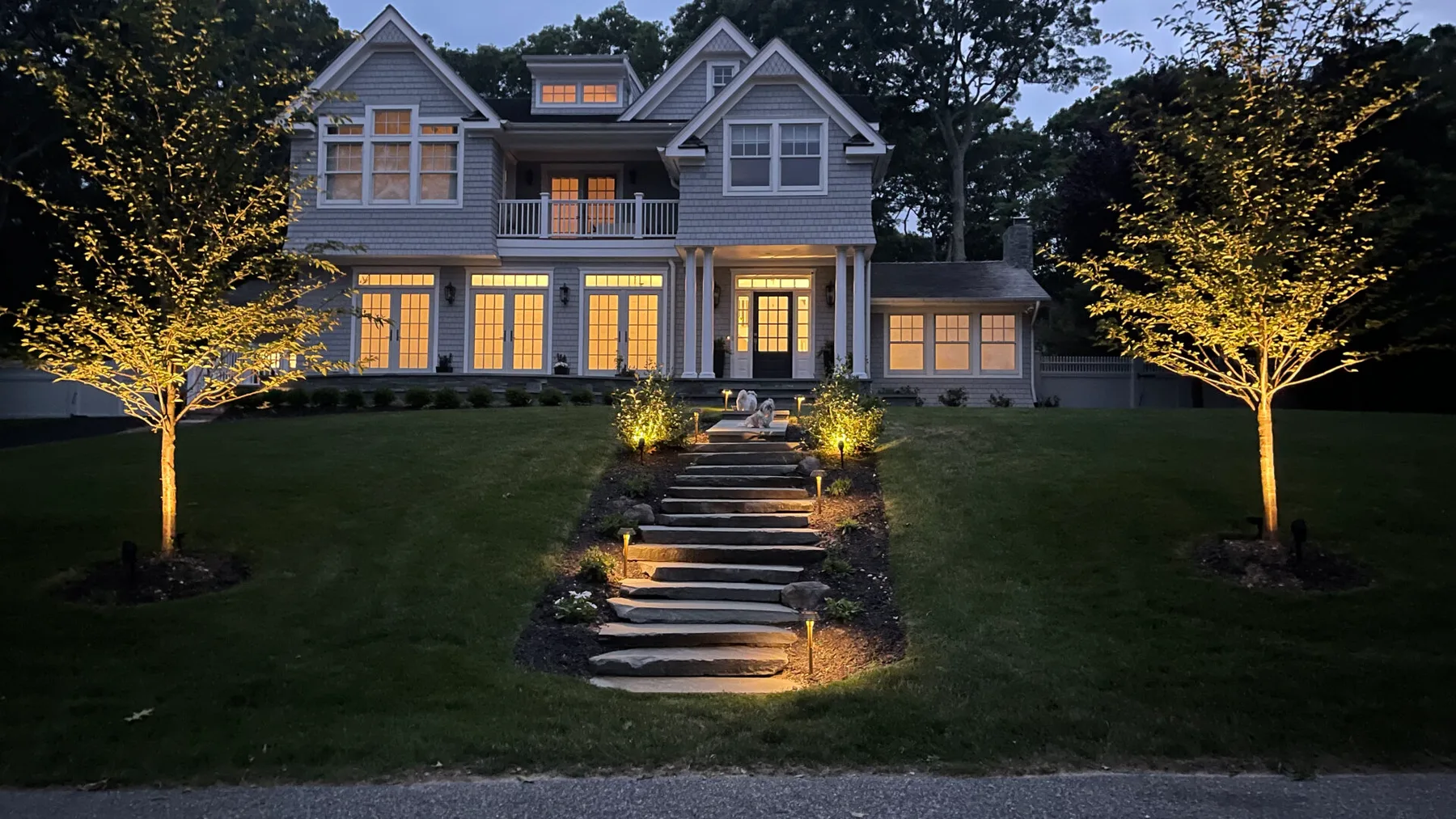 A large house glows with warm lights above a landscaped front lawn.