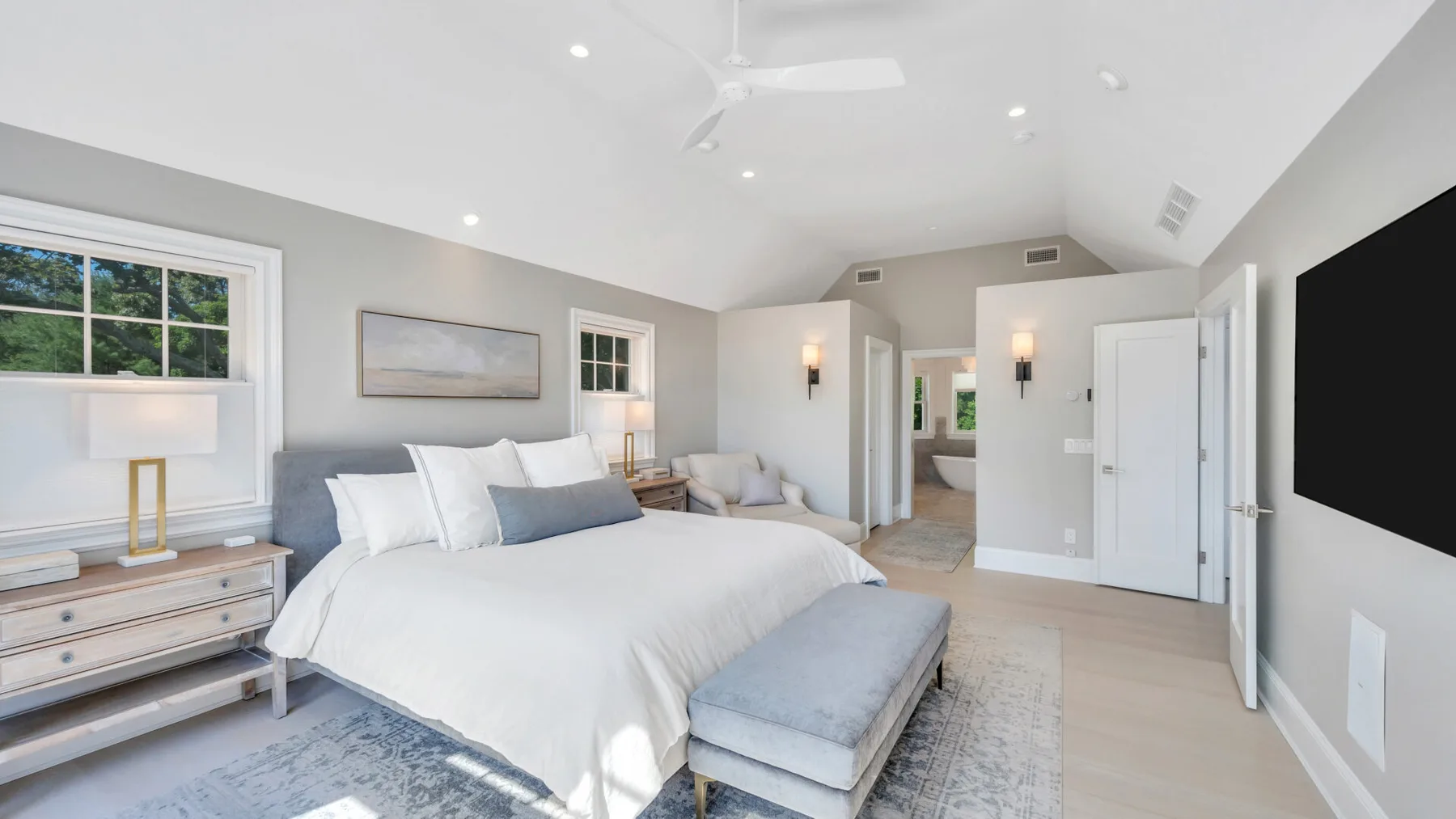 A bright bedroom with a large bed and a blue upholstered bench.