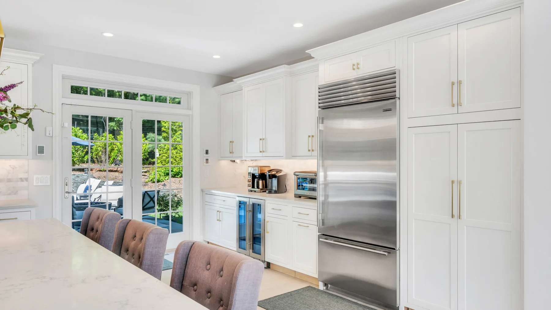 A bright white kitchen with a large island and stainless steel refrigerator.