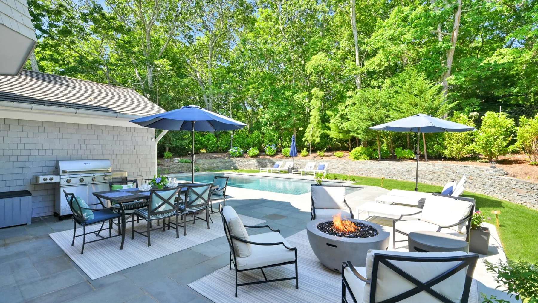 A backyard patio with a swimming pool, outdoor seating, and a fire pit.