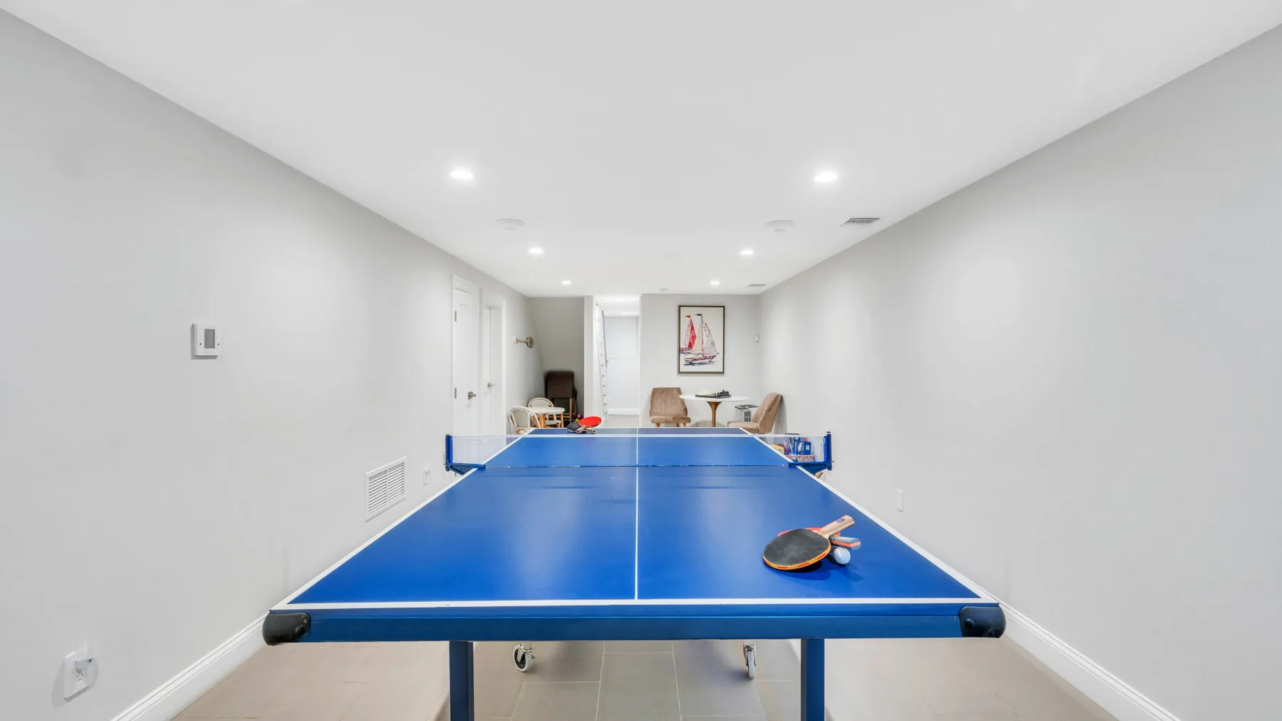 A blue ping-pong table fills a bright, narrow indoor recreation room.