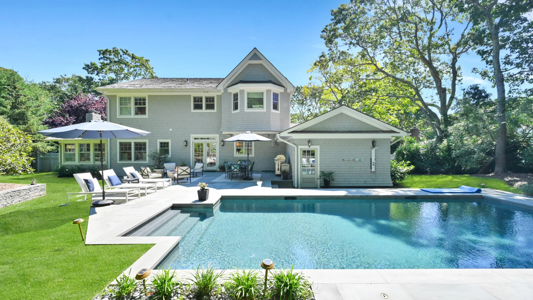 A backyard swimming pool sits beside a two-story house and patio.