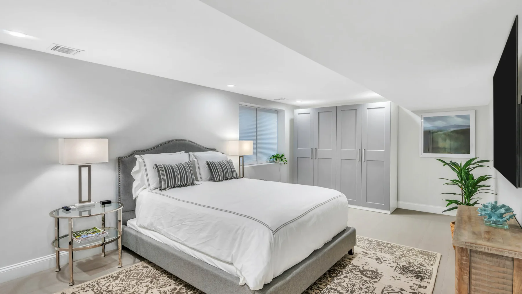A bright bedroom with a neatly made bed, bedside lamps, and a patterned rug.