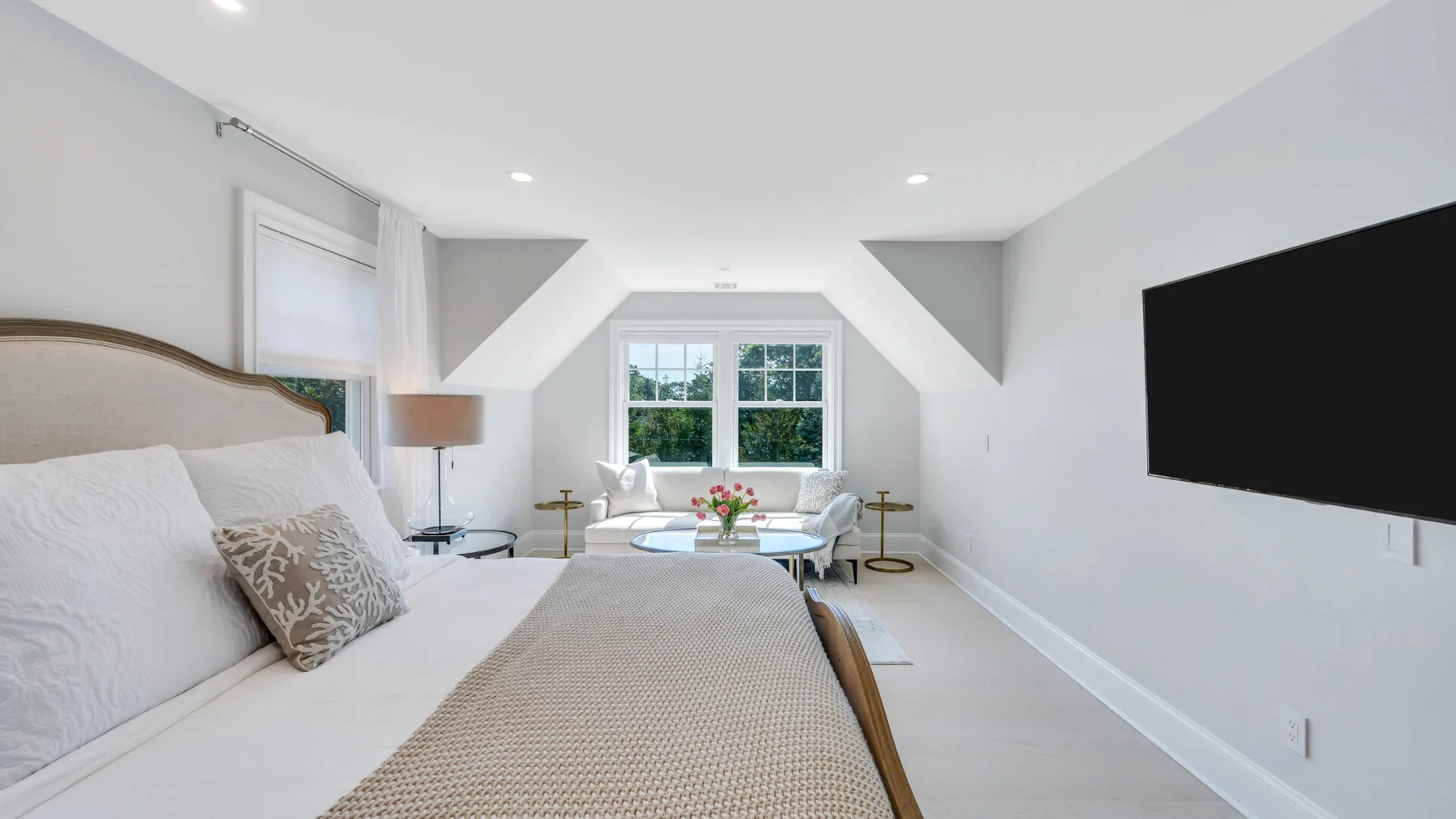 A bright bedroom with a bed, seating area, and wall-mounted television.