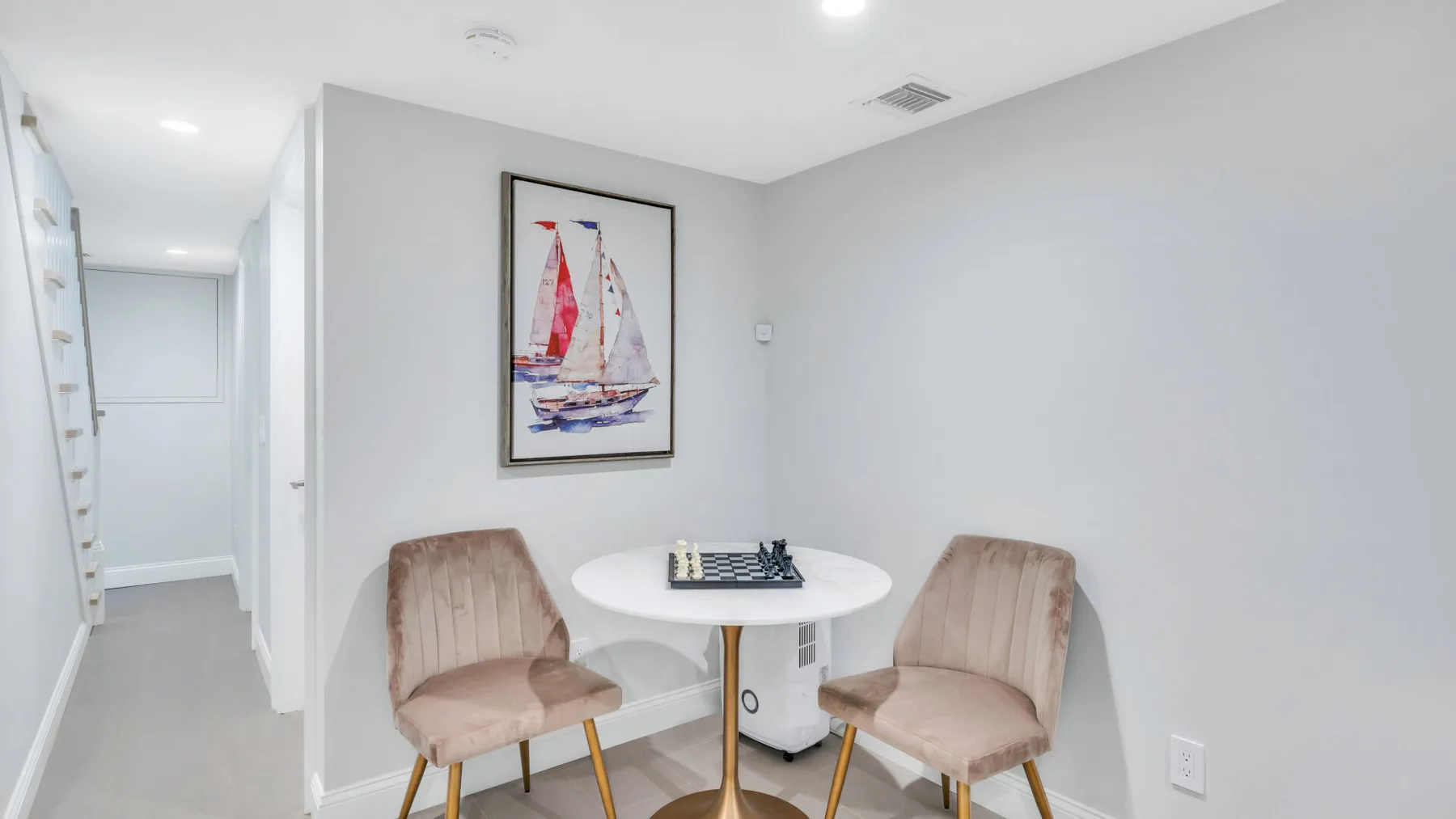 A small dining area with a round table and framed sailboat artwork.