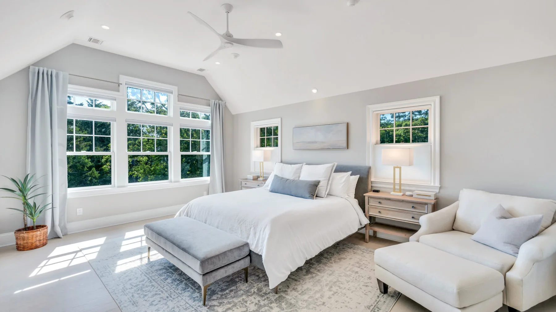 A bright bedroom with a large bed, wide windows, and a pale area rug.