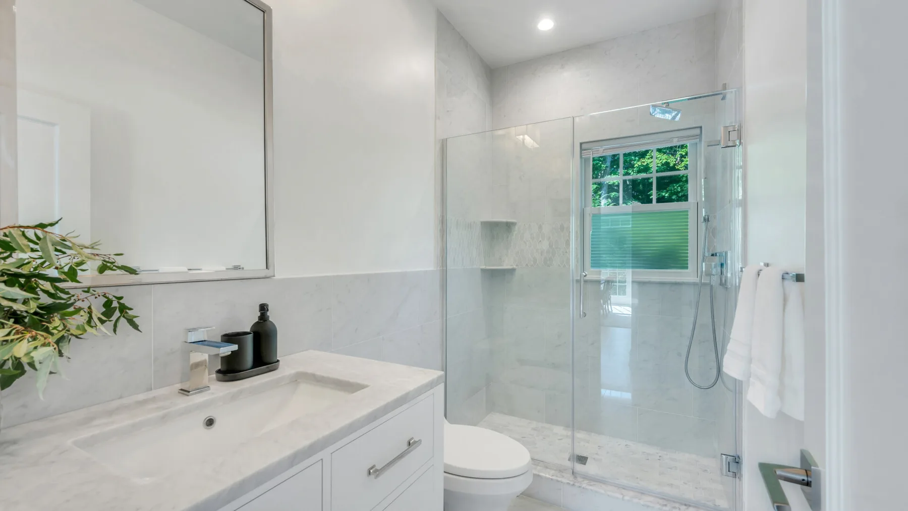 A bright bathroom with a vanity, toilet, and glass shower.