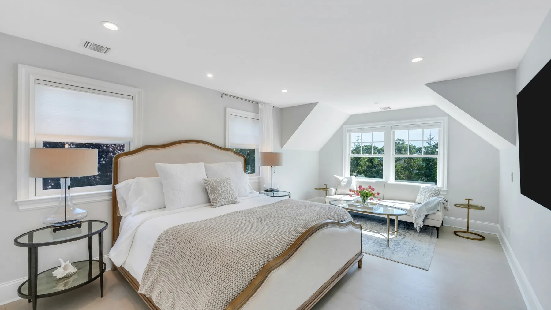 A bright bedroom with a large bed and a sitting area by the windows.