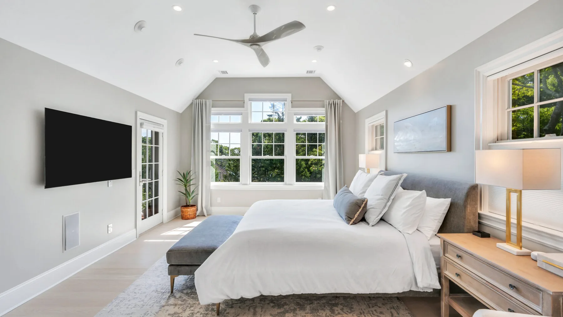 A bright bedroom with a large bed and windows overlooking greenery.