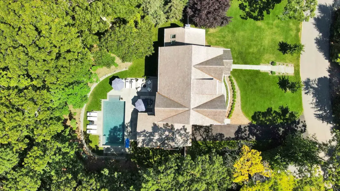 An aerial view of a house surrounded by trees, with a swimming pool beside it.