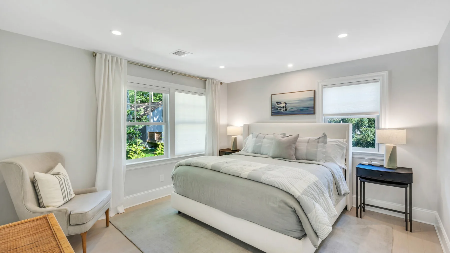 A bright bedroom with a neatly made bed and windows overlooking greenery.