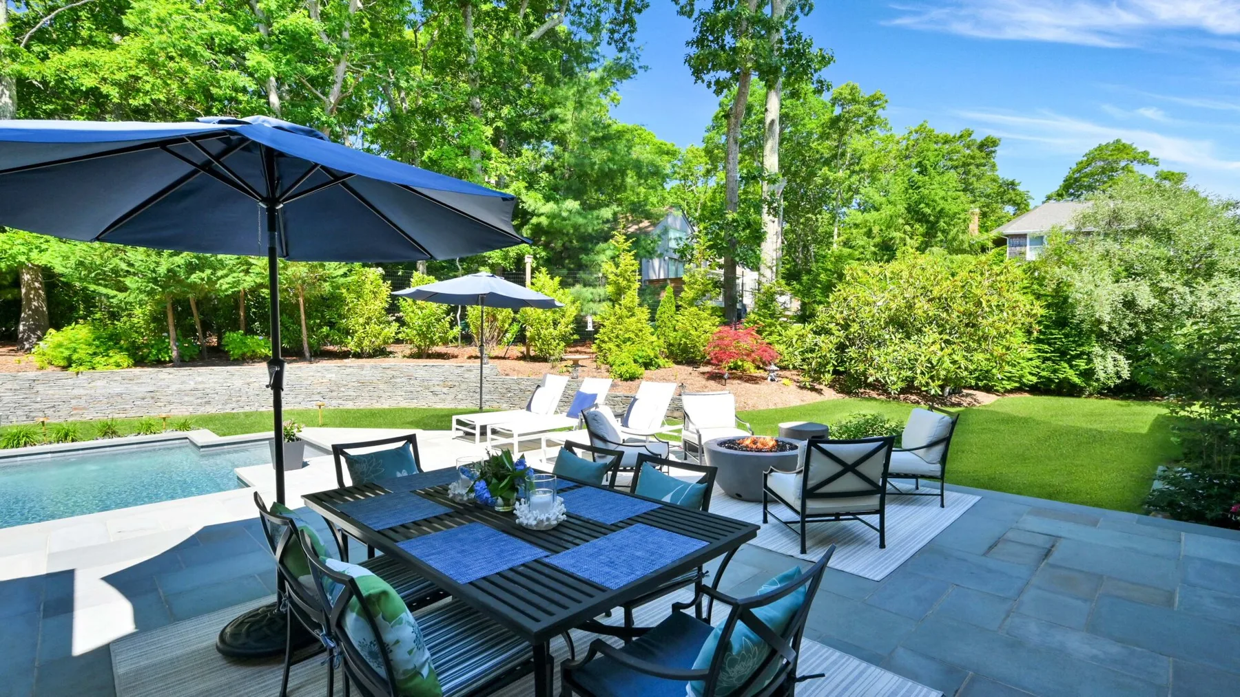 An outdoor patio dining area beside a swimming pool, with tables and umbrellas.