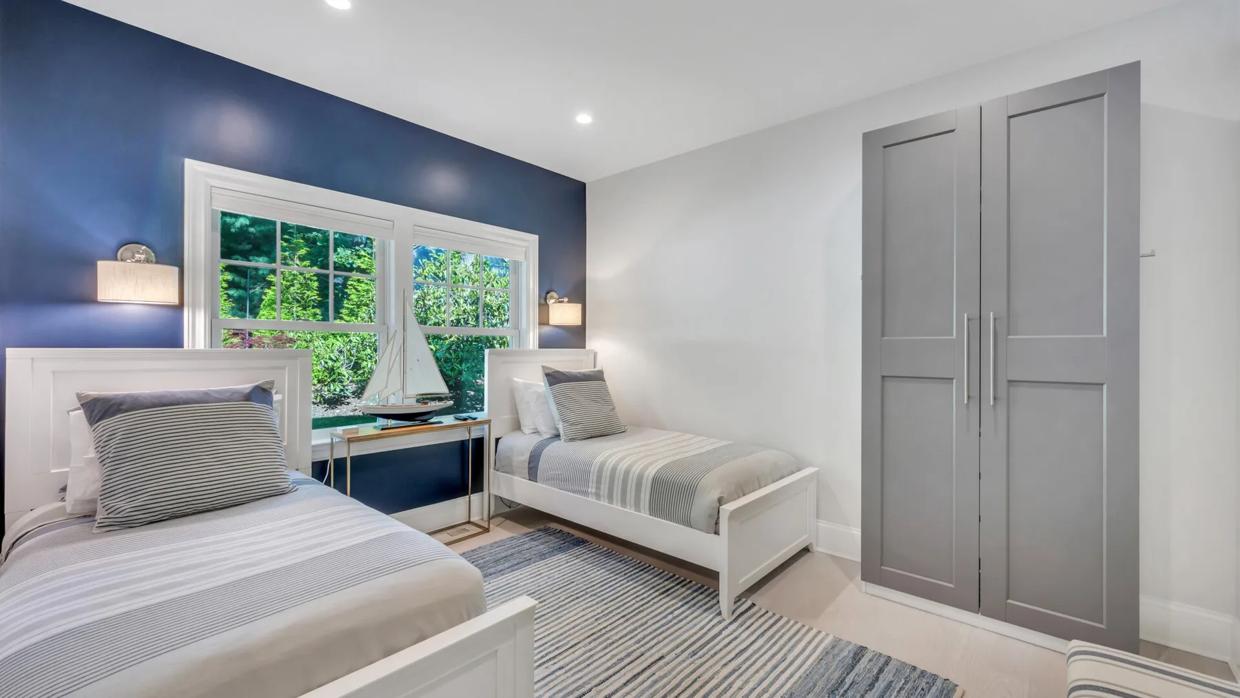 A bedroom with two beds, windows, and a gray wardrobe.