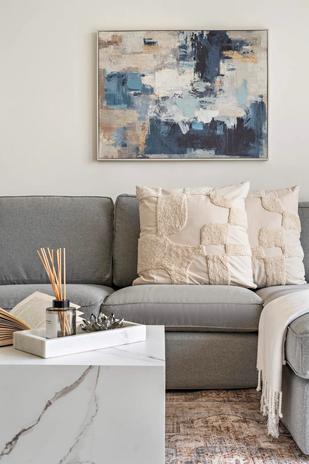 Una zona de estar presenta un sofá gris, cojines decorativos y arte abstracto en la pared.