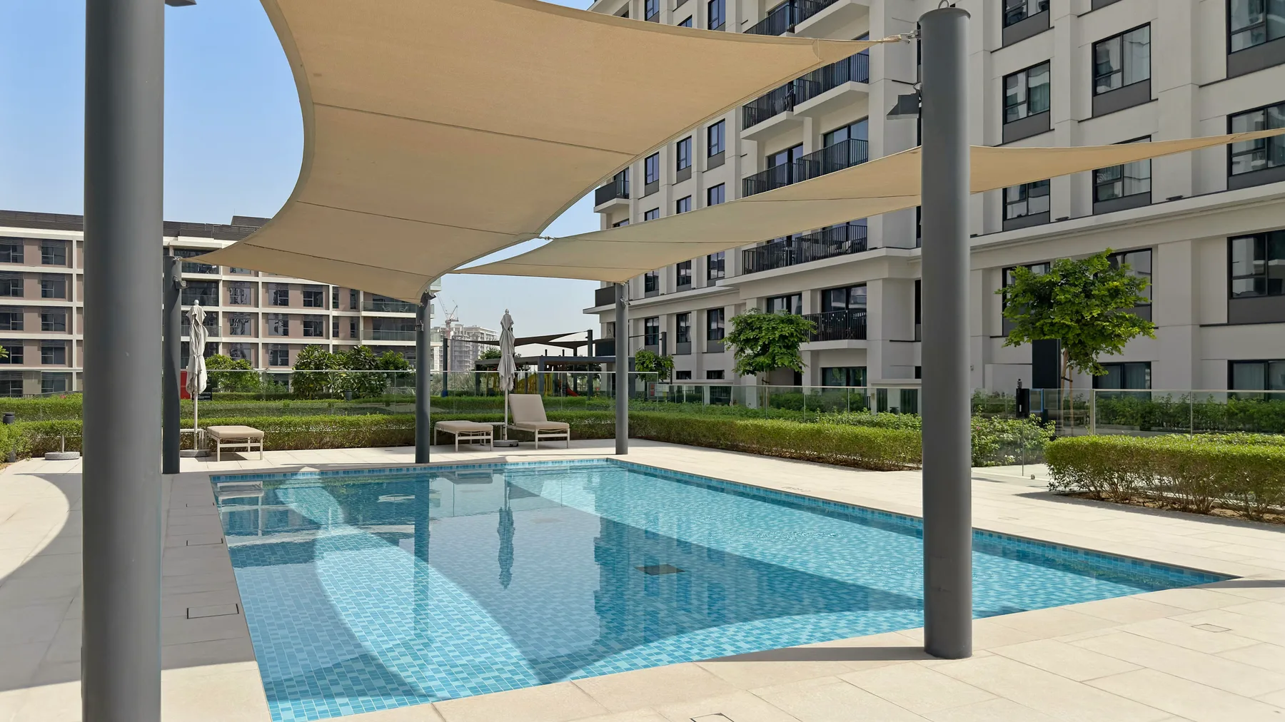 Una piscina al aire libre está bajo toldos de sombra junto a un edificio moderno de apartamentos.