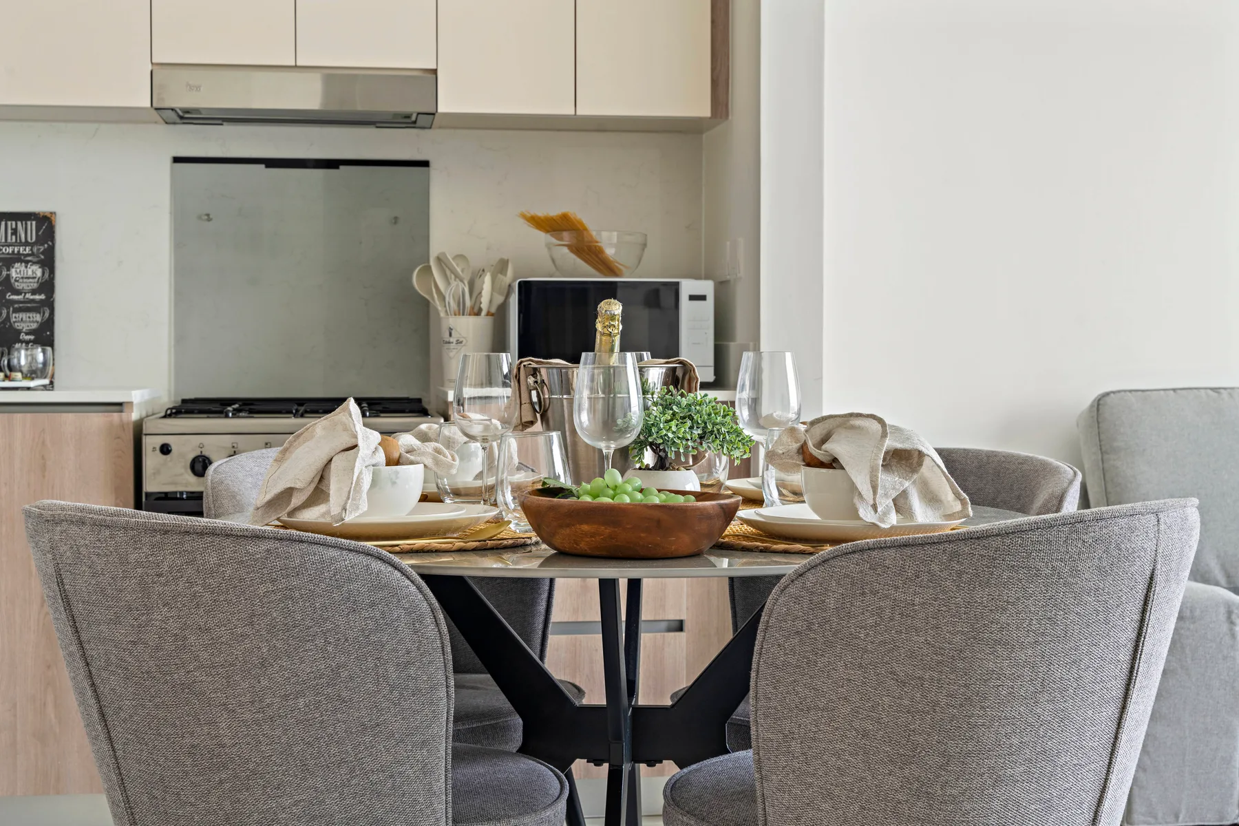 Una mesa de comedor está puesta con copas y platos frente a una cocina.