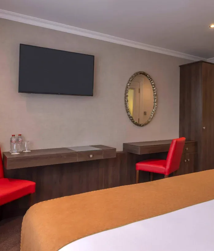 Hotel bedroom with red chairs and mounted TV.