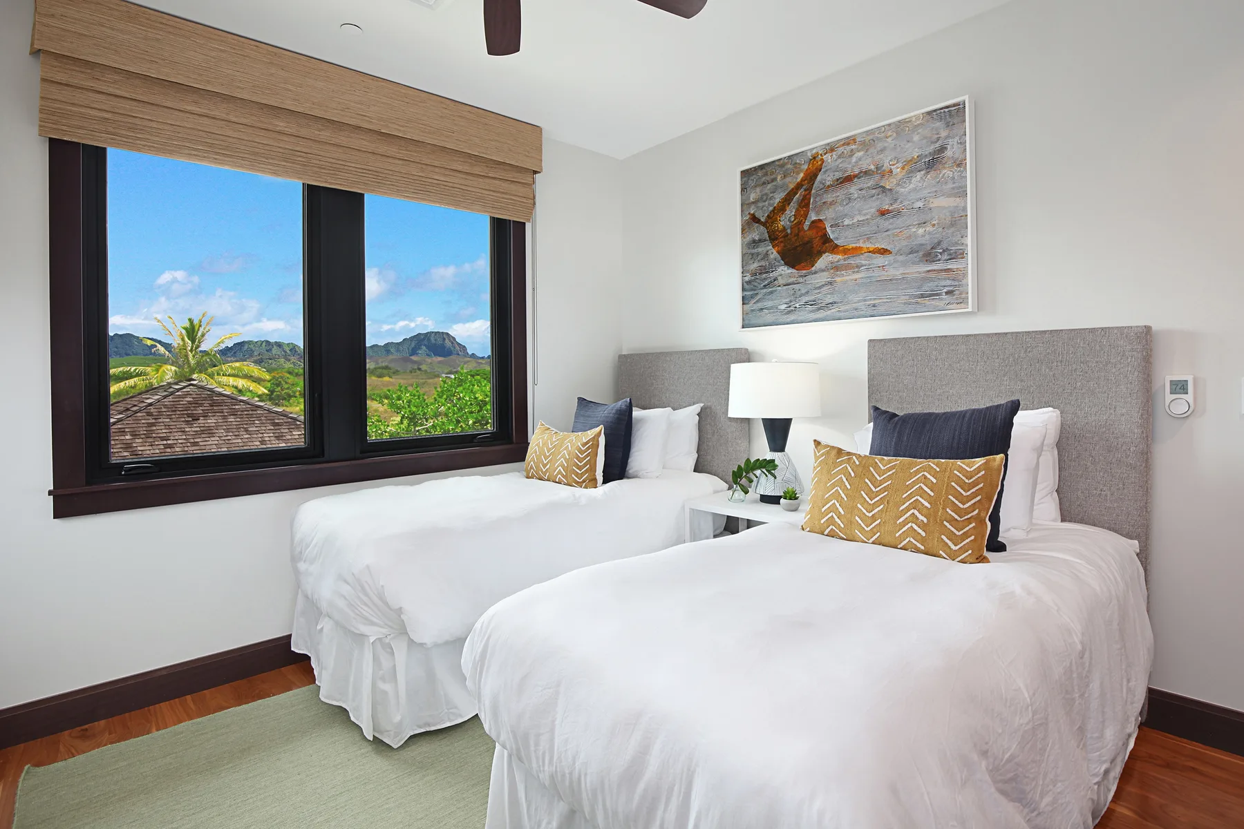 A bedroom with two beds beside a large window overlooking green hills.