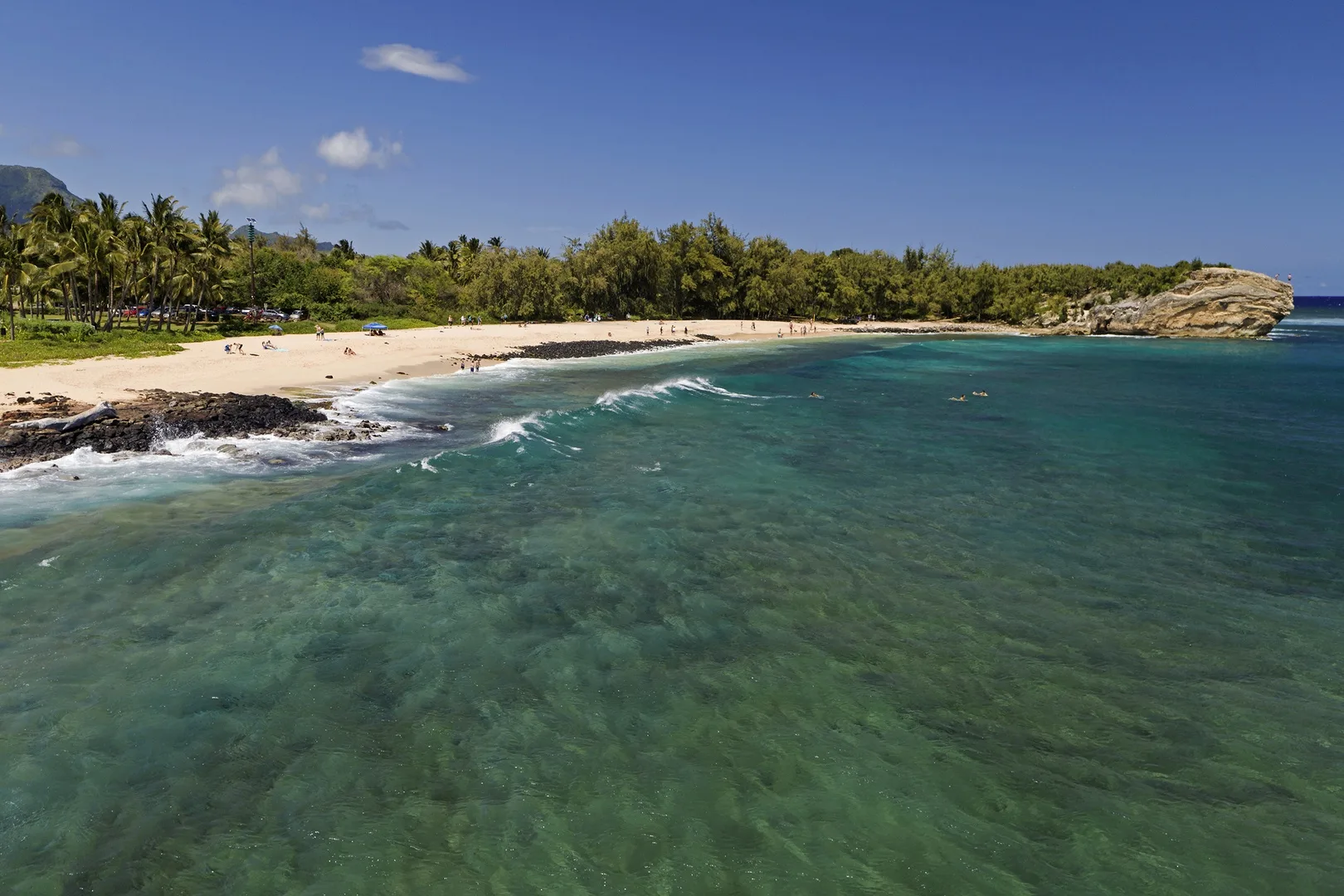 A sandy beach curves along clear turquoise water beneath a blue sky.