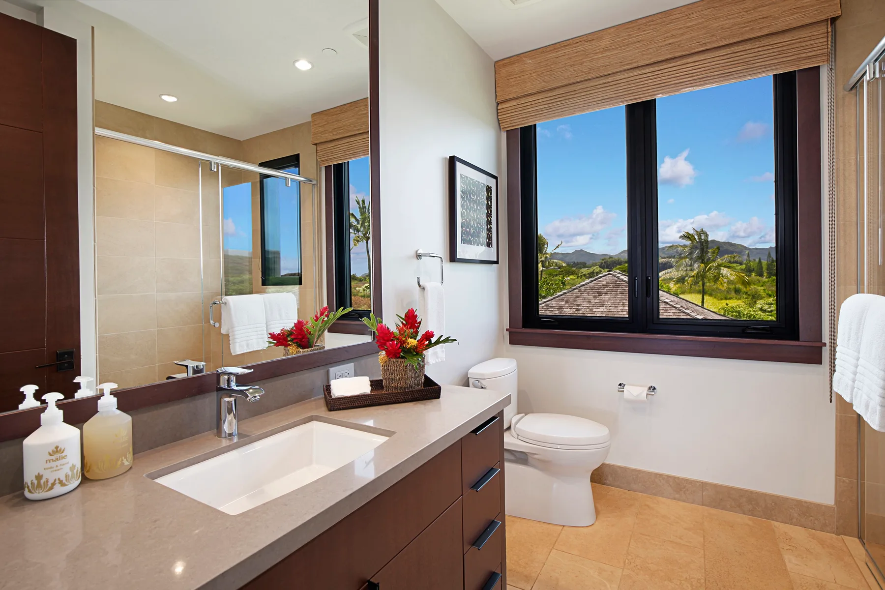 A bright bathroom with a vanity, toilet, and a large window overlooking greenery.